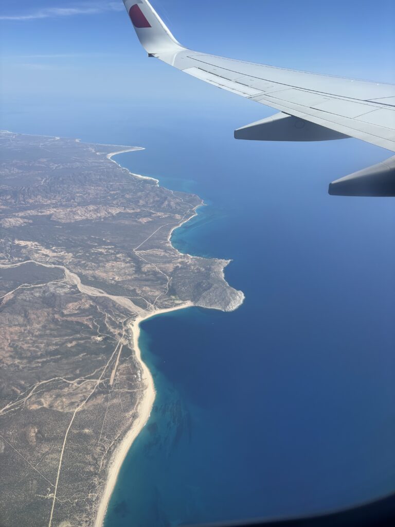 Airplane wing over the ocean approaching Cabo San Lucas.